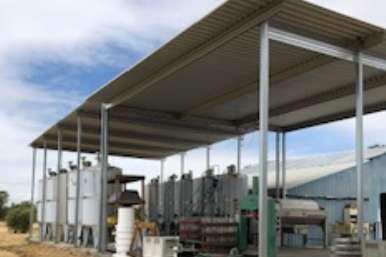 Open-sided winery crush pad cover shading equipment near vineyard production building
